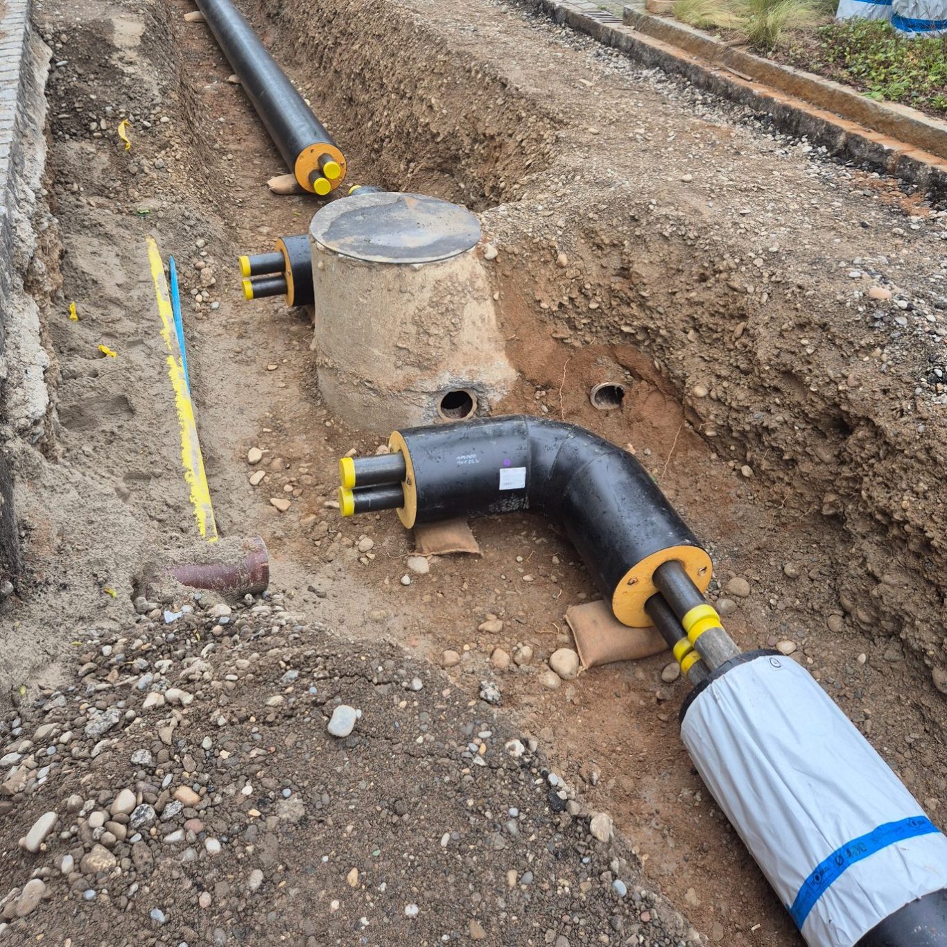 Eine offene Baugrube im Kreuzungsbereich mit freigelegten Bestandsleitungen und neuer Nahwärmeleitung.