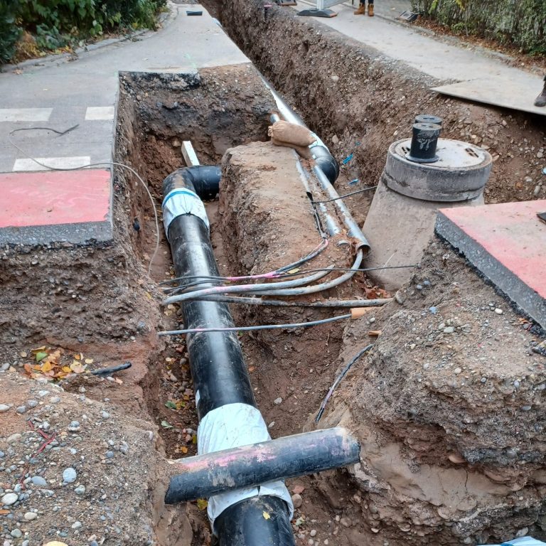 Eine offene Baugrube im Kreuzungsbereich mit freigelegten Bestandsleitungen und neuer Nahwärmeleitung. 