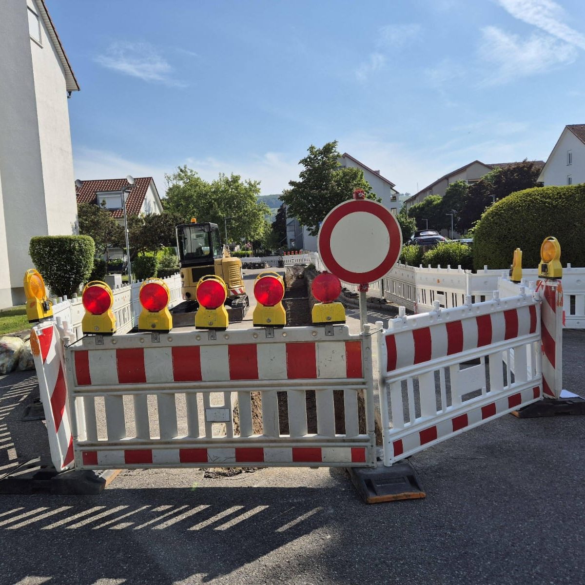 Baustelle mit Vollsperrun, welche durch rot-weiße Bauzäune und Warnlichtern auf einer Anwohnerstraße abgesperrt ist.