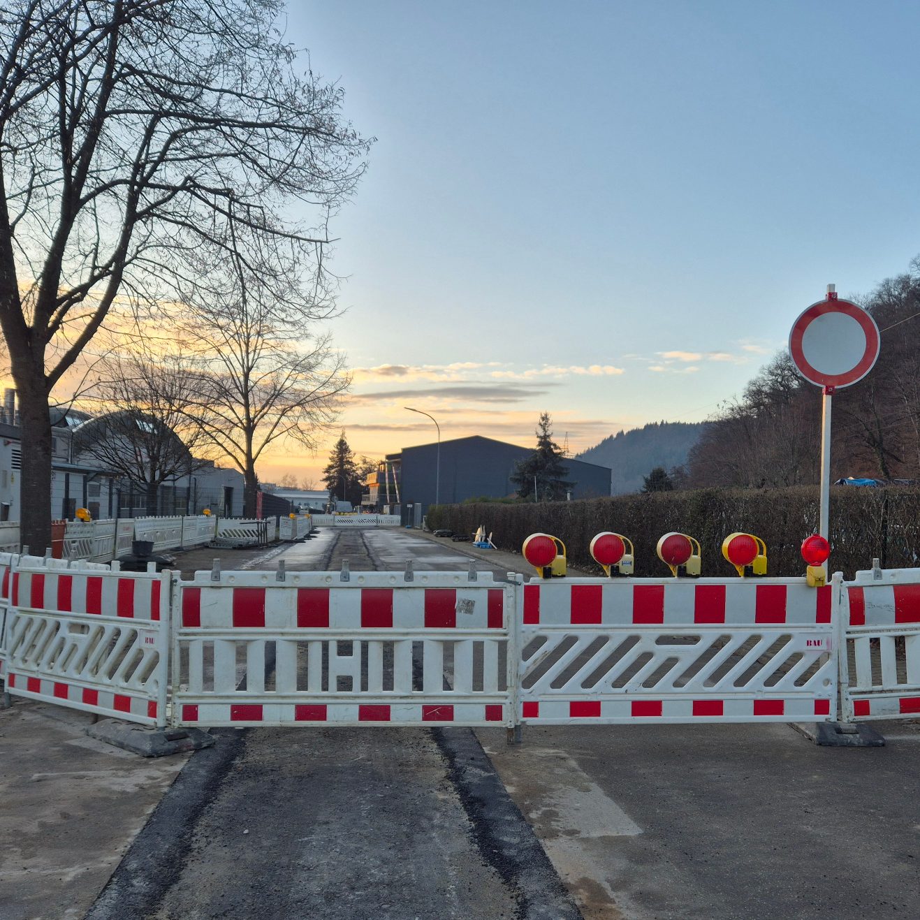 Baustelle mit Vollsperrun, welche durch rot-weiße Bauzäune und Warnlichtern auf einer Anwohnerstraße abgesperrt ist.