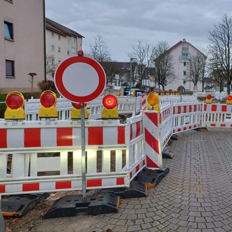 Baustelle mit Vollsperrun, welche durch rot-weiße Bauzäune und Warnlichtern auf einer Anwohnerstraße abgesperrt ist.