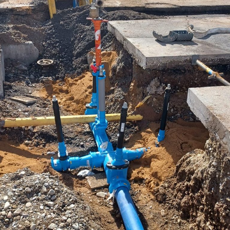 Blaue Formstücke Gewerk Wasser und gelbe Gasleitung in einer Baustelle mit freigelegtem Erdreich.
