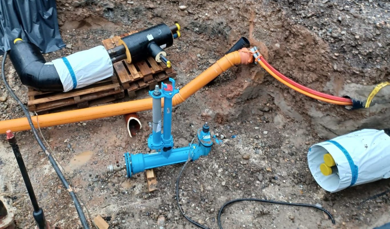 Offfener Tiefbaugraben mit laufenden Rohrleitungsarbeiten für die Gewerke Nahwärme, Wasser, Breitband und Entwässerung.